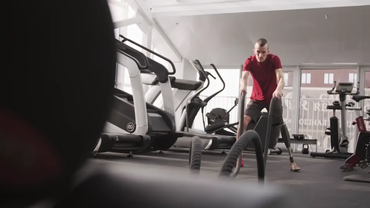 Athlete performing battle-rope training in a bright gym.