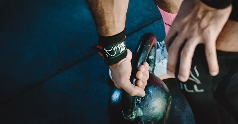 Muscular athlete lifting kettlebell during workout session, showcasing strength and fitness.