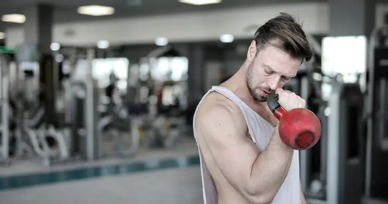 An athletic man working out with a kettlebell in a gym setting, emphasizing strength training.