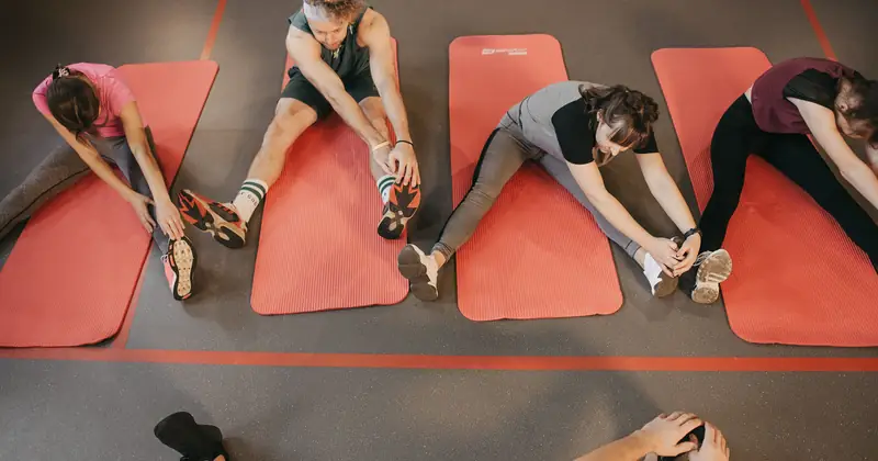 Four people stretching on red mats during a group exercise session indoors.