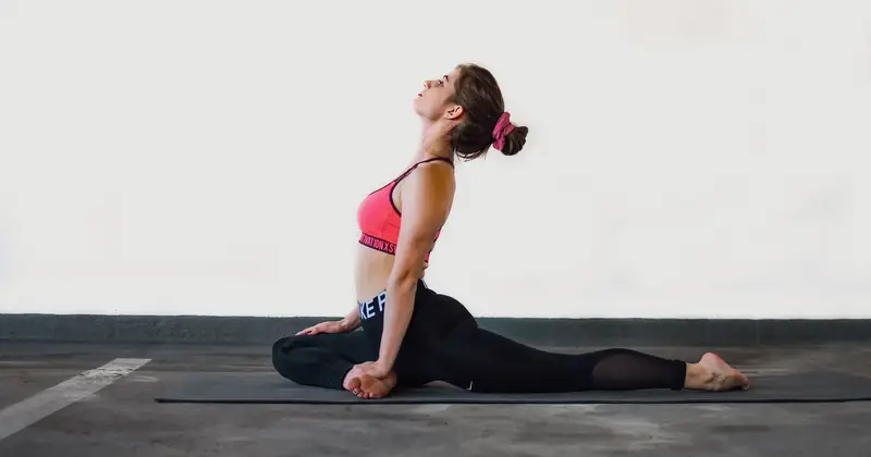 Young woman in yoga pose on mat indoors showcasing flexibility and focus.