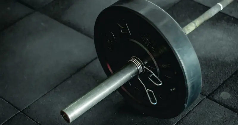 Detailed view of a barbell with heavy weights resting on a dark gym floor mat.
