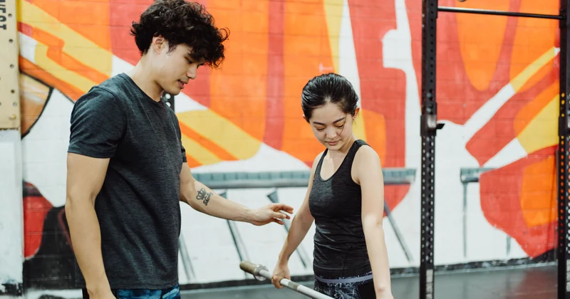 Coach helping a woman learn barbell lifting technique in a bright gym.